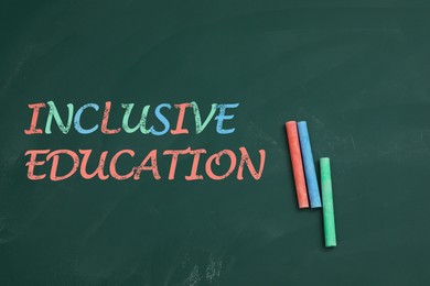 Image of Phrase INCLUSIVE EDUCATION and colorful chalks on green board, flat lay