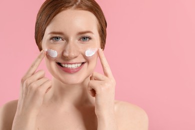 Photo of Smiling woman with freckles and cream on her face against pink background. Space for text