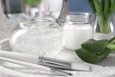 Photo of Jar of natural gel, burning candle, makeup brushes and fresh aloe leaves on white tray, closeup
