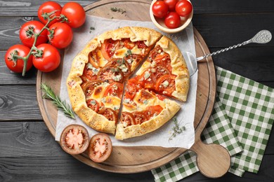 Photo of Tasty galette with tomato and cheese (Caprese galette) on black wooden table, top view