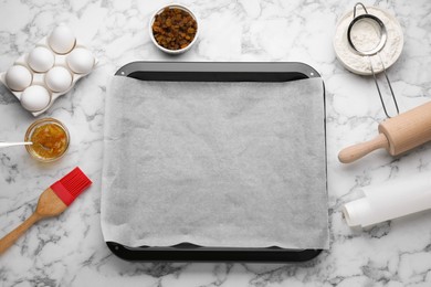 Photo of Baking pan with parchment paper and ingredients on white marble table, flat lay