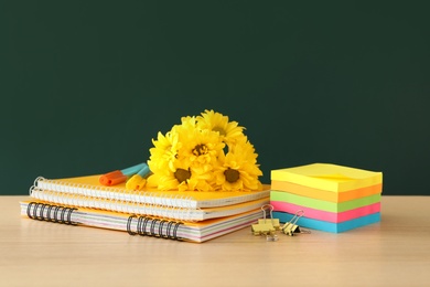 Photo of Set of stationery and flowers on wooden table near chalkboard. Teacher's Day