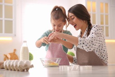 Mother and daughter making dough at table in kitchen