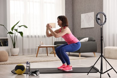 Photo of Happy sports blogger streaming online fitness lesson with smartphone at home