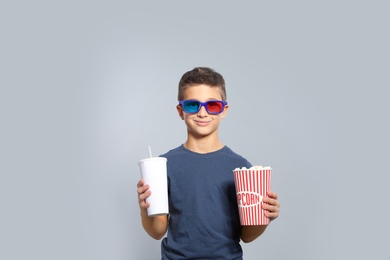 Boy with 3D glasses, popcorn and beverage during cinema show on grey background