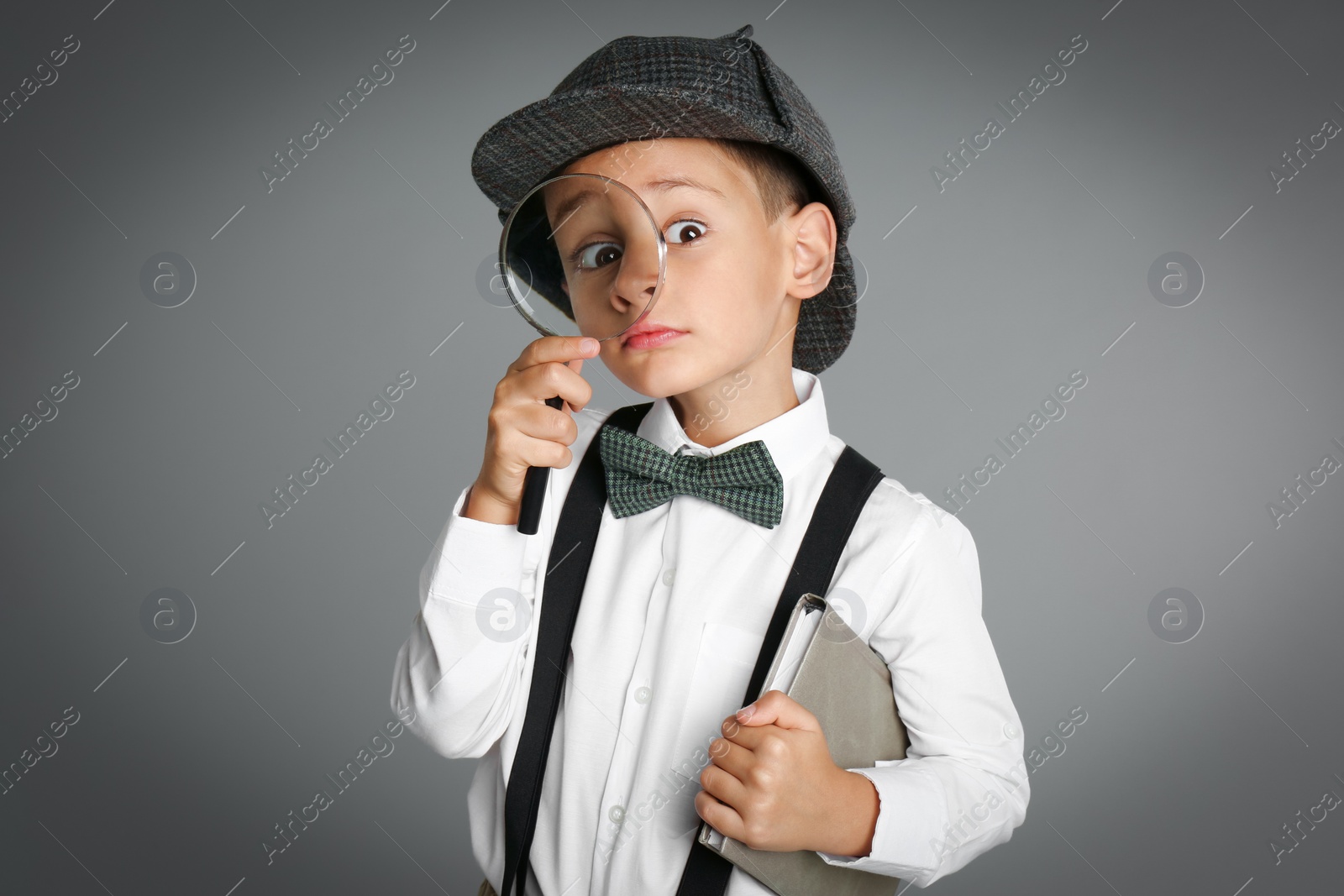 Photo of Little boy with magnifying glass playing detective on grey background