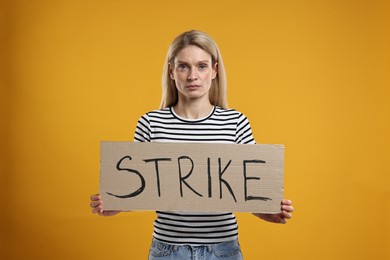 Photo of Woman holding cardboard banner with word Strike on orange background