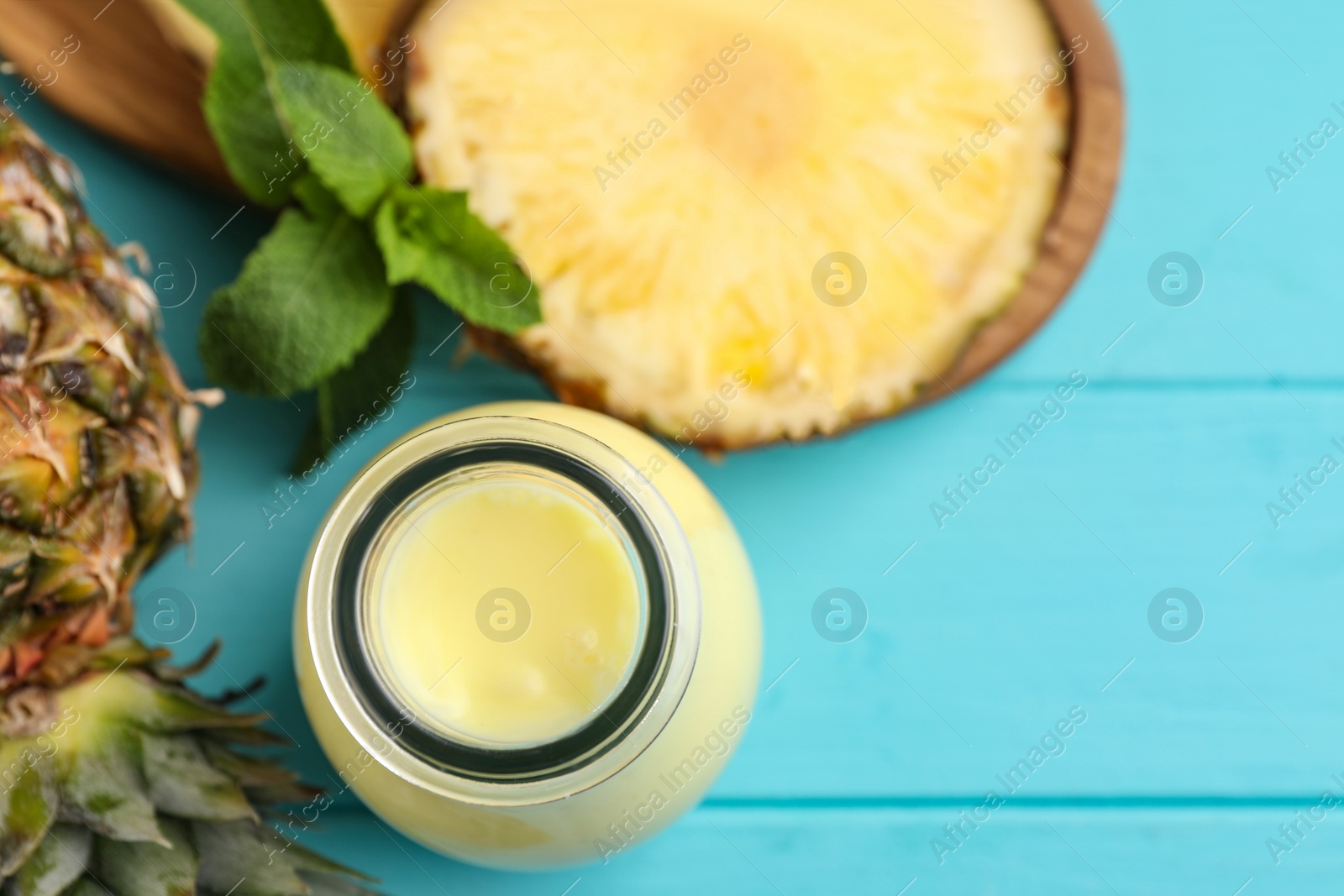Photo of Tasty pineapple smoothie in bottle, mint and fruit on light blue wooden table, flat lay. Space for text