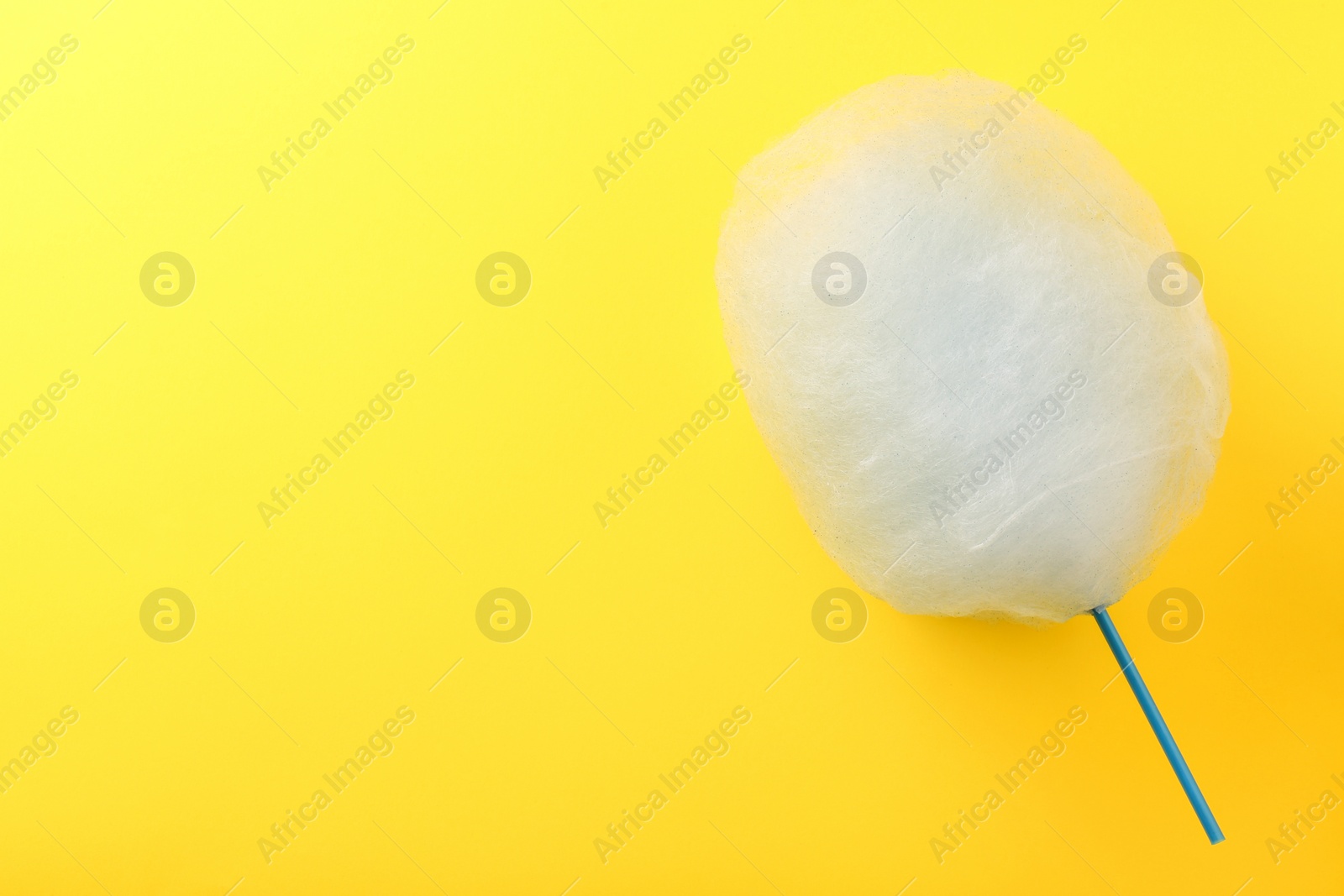 Photo of Sweet light blue cotton candy on yellow background, top view. Space for text