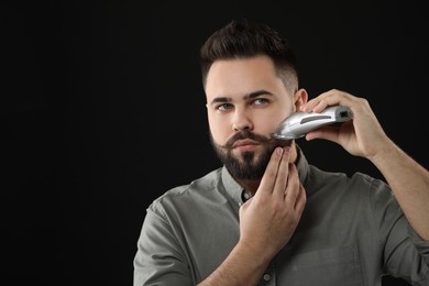 Photo of Handsome young man trimming beard on black background. Space for text