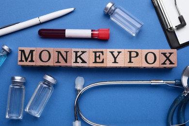 Flat lay composition with word Monkeypox made of wooden cubes and medical supplies on blue background