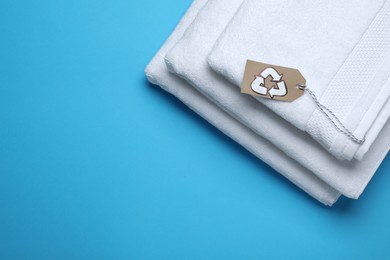 Photo of Stacked towels with recycling label on light blue background, top view. Space for text