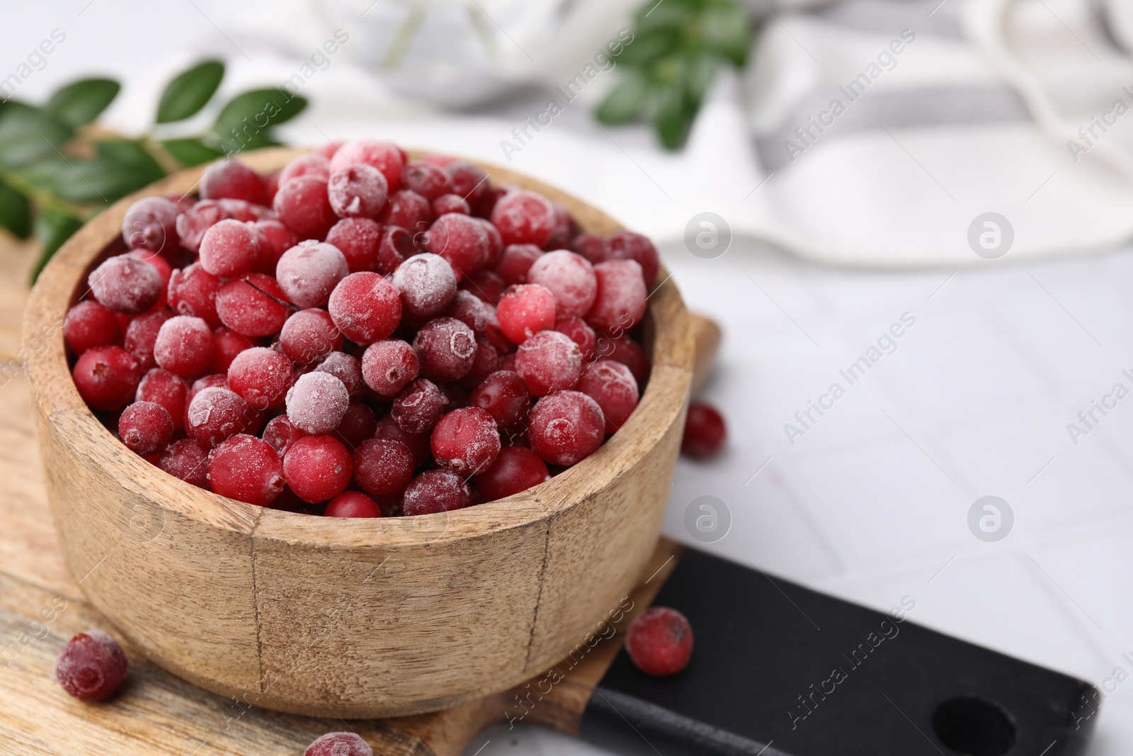 Photo of Frozen red cranberries in bowl on white tiled table, closeup. Space for text