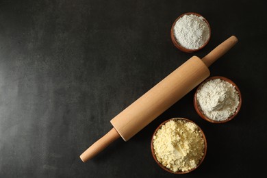 Photo of Rolling pin and different types of flour on black table, flat lay. Space for text