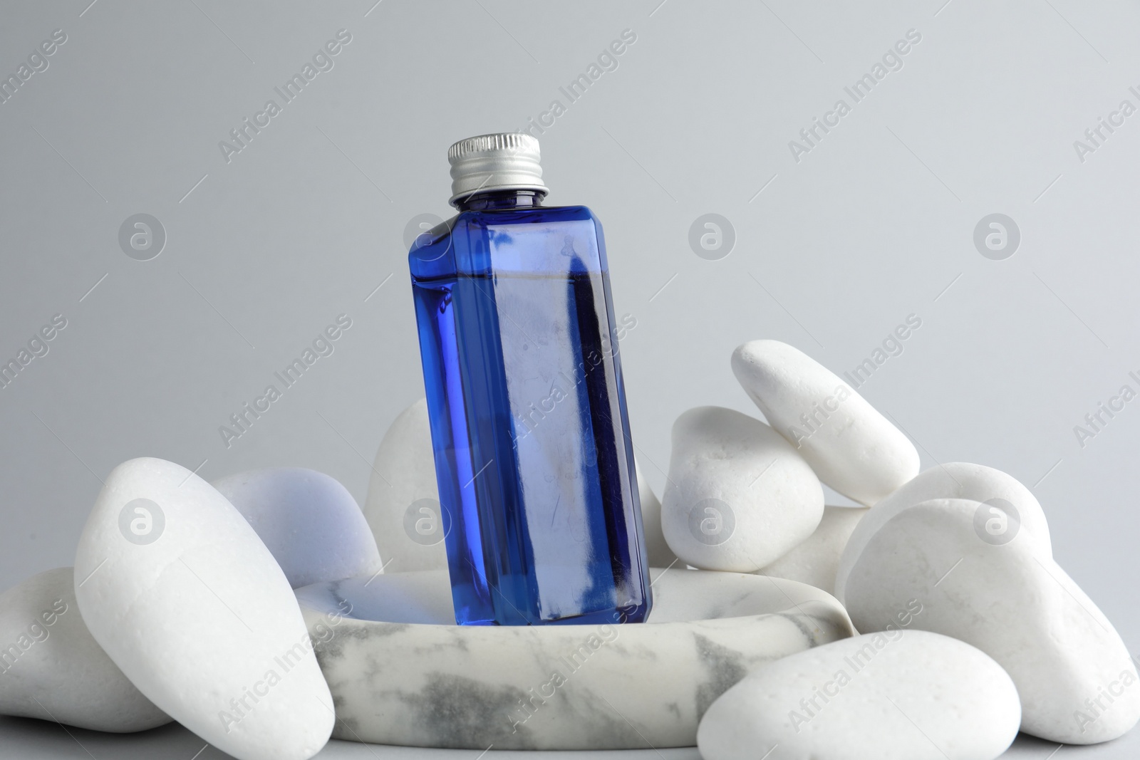 Photo of Bottle of cosmetic product and stones on light grey background