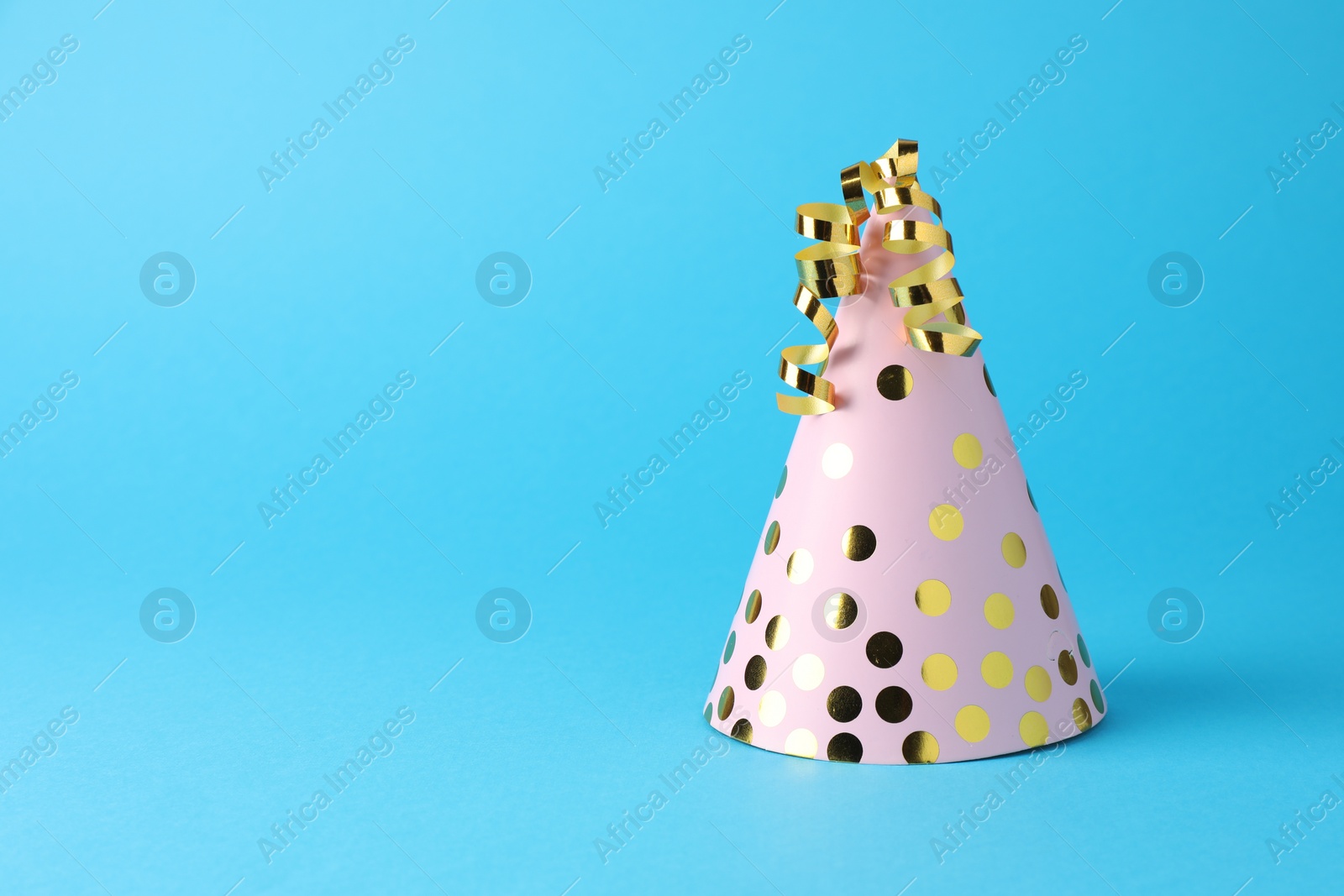 Photo of Pink party hat and serpentine streamers on light blue background, space for text