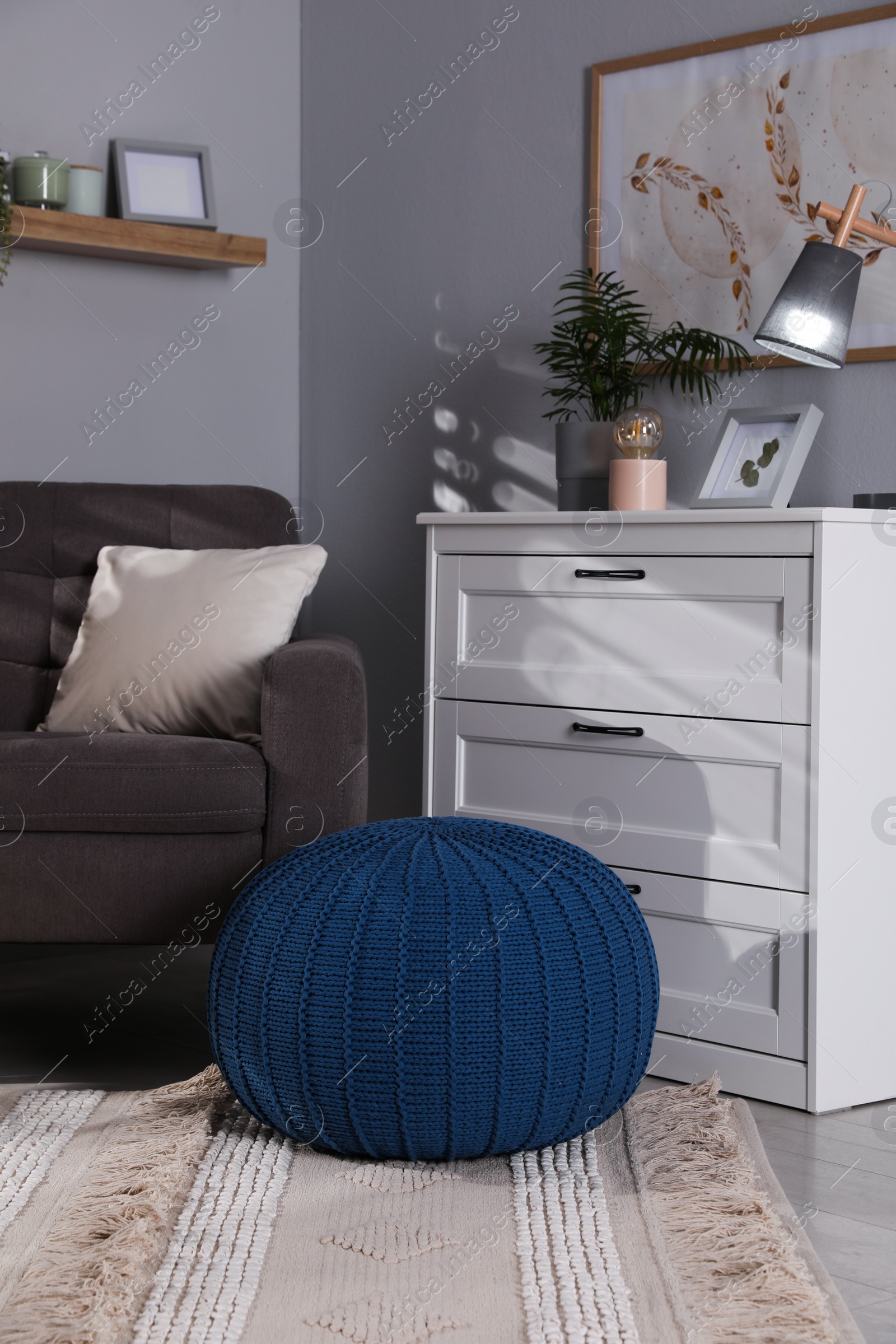 Photo of Stylish knitted pouf and chest of drawers in room. Home design
