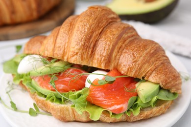 Tasty croissant with salmon, avocado, mozzarella and lettuce on table, closeup