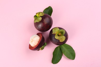 Photo of Fresh ripe mangosteen fruits with green leaves on pink background, flat lay