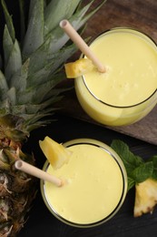 Photo of Tasty pineapple smoothie, mint and fruit on black table, flat lay