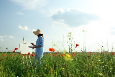 Photo of Woman painting on easel in beautiful poppy field