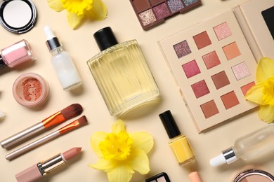 Photo of Flat lay composition with different makeup products and beautiful spring flowers on beige background