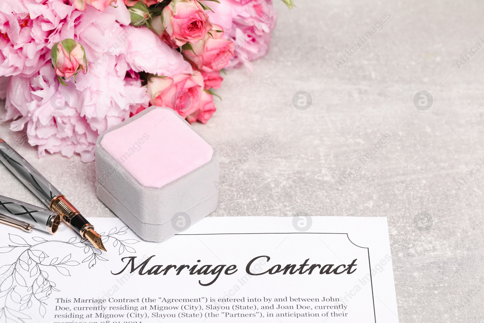 Photo of Marriage contract, fountain pen, jewelry box and flowers on grey table