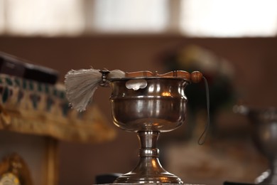 Photo of Silver vessel with holy water and brush on stand in church. Baptism ceremony