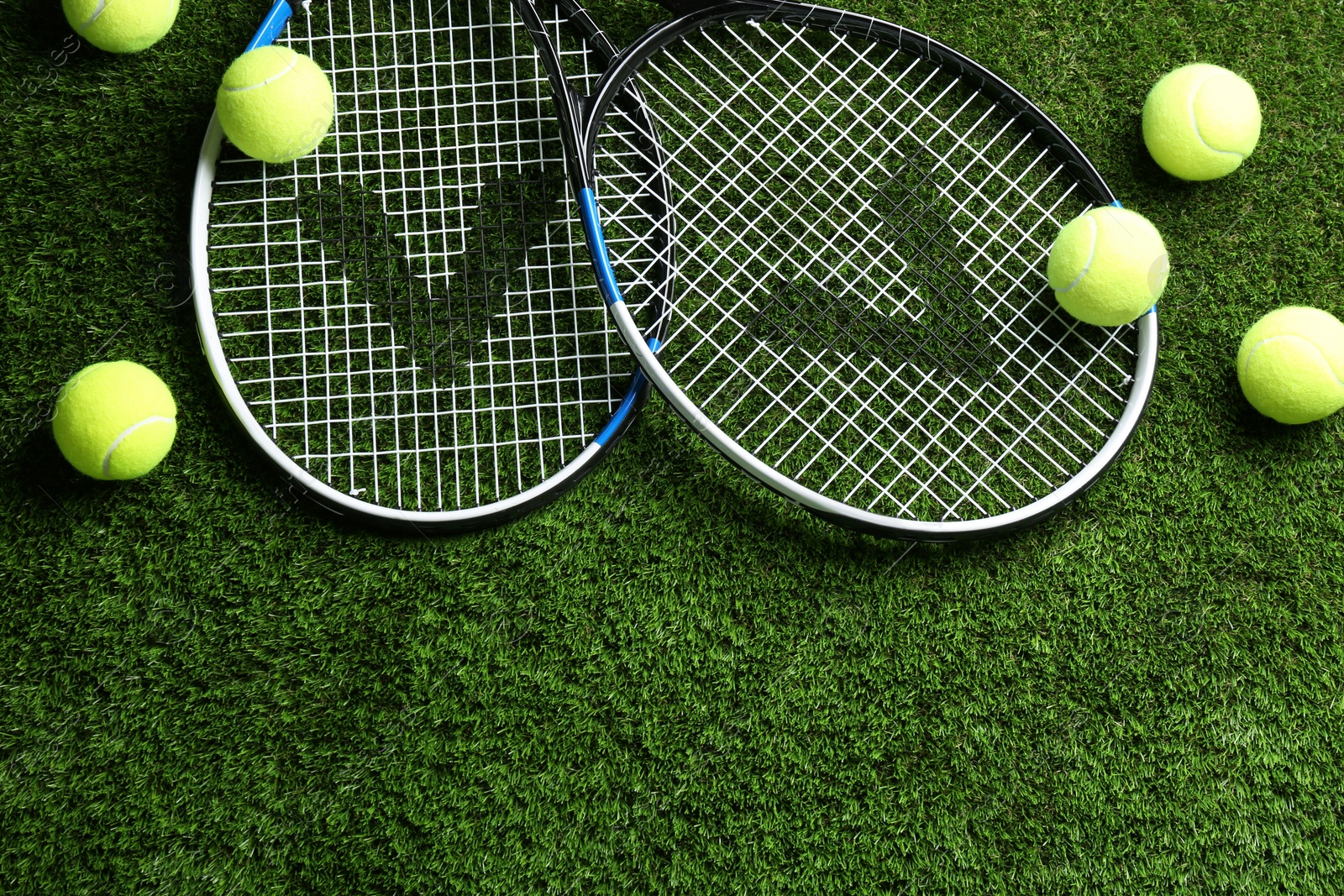 Photo of Tennis rackets and balls on green grass, flat lay. Space for text