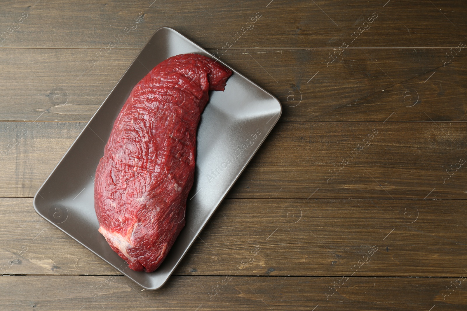 Photo of Plate with piece of raw meat on wooden table, top view. Space for text
