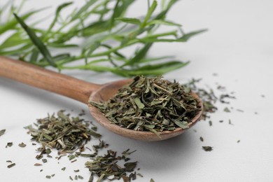 Photo of Spoon of dry tarragon on white table, closeup