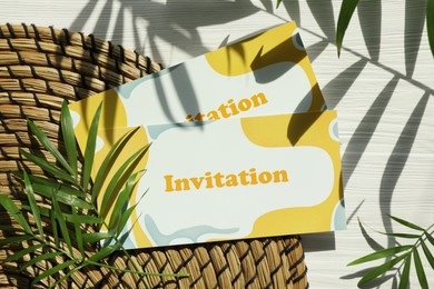 Photo of Beautiful cards with word Invitation and palm leaves on white wooden table, flat lay