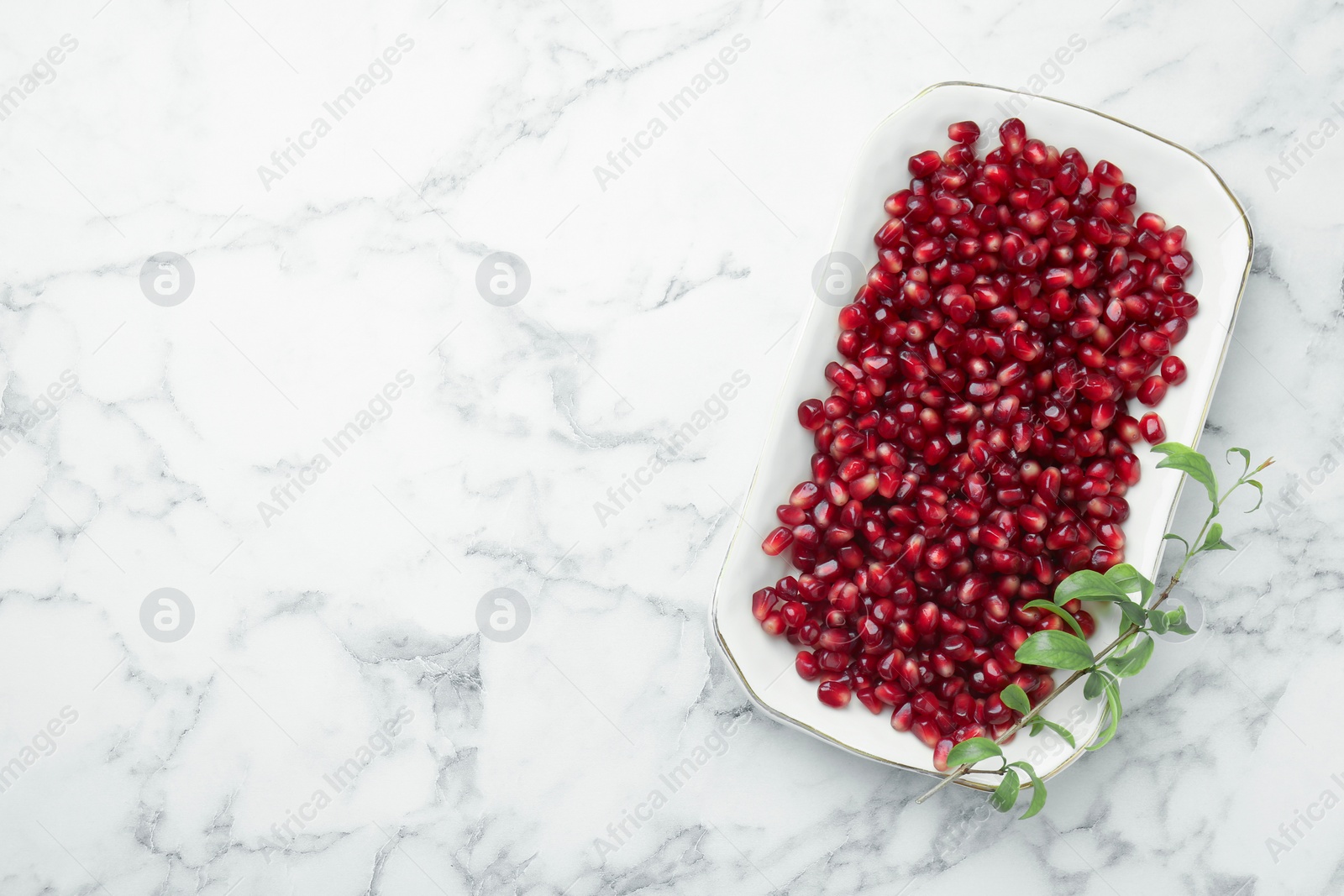 Photo of Ripe juicy pomegranate grains and green leaves on white marble table, top view. Space for text