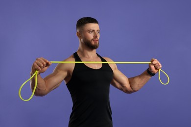 Muscular man exercising with elastic resistance band on purple background