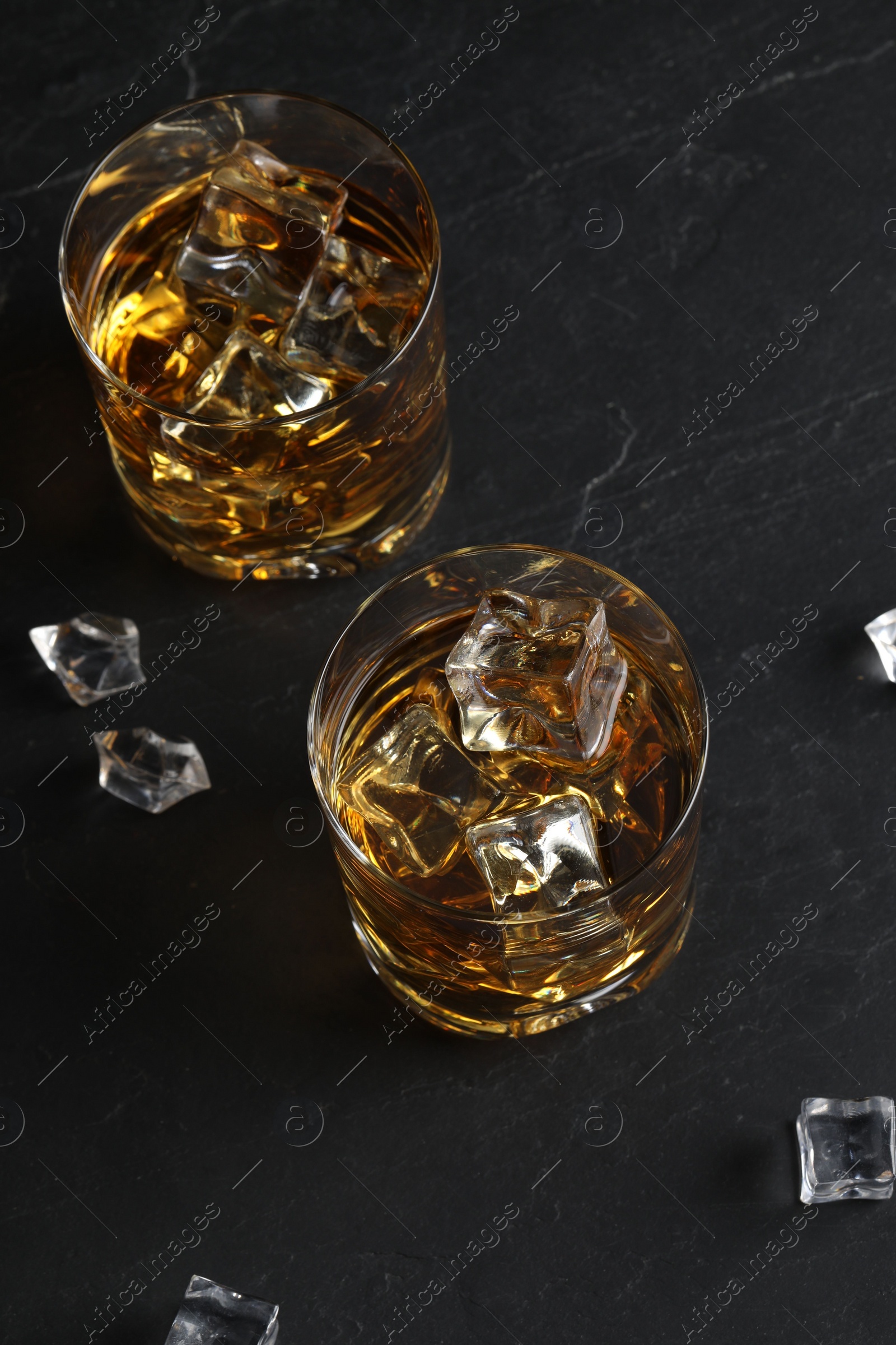 Photo of Whiskey and ice cubes in glasses on black table, above view
