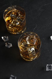 Whiskey and ice cubes in glasses on black table, above view