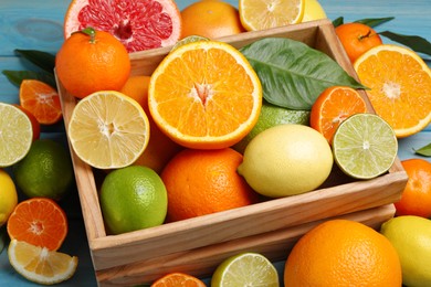 Photo of Different ripe citrus fruits with green leaves on light blue wooden table