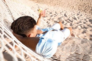 Photo of Man with refreshing cocktail relaxing in hammock on beach
