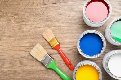 Open cans with paint and brushes on wooden background, flat lay