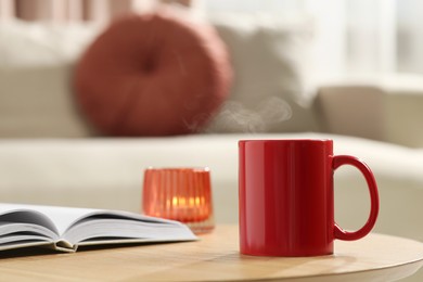 Photo of Red mug, open book and burning candle on wooden table indoors. Mockup for design