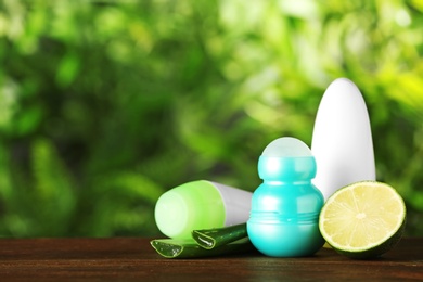 Photo of Natural deodorants with aloe and lime on wooden table against blurred green background. Space for text