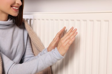 Photo of Woman warming hands near heating radiator, closeup