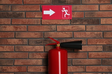 Photo of Fire extinguisher and emergency exit sign on brick wall indoors
