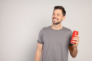 Photo of Happy man holding red tin can with beverage on light grey background. Space for text