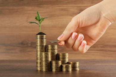 Woman putting coin onto stack with green sprout at wooden table, closeup. Investment concept