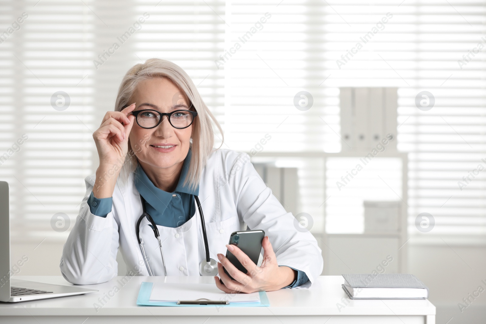 Photo of Mature female doctor with smartphone at table in office