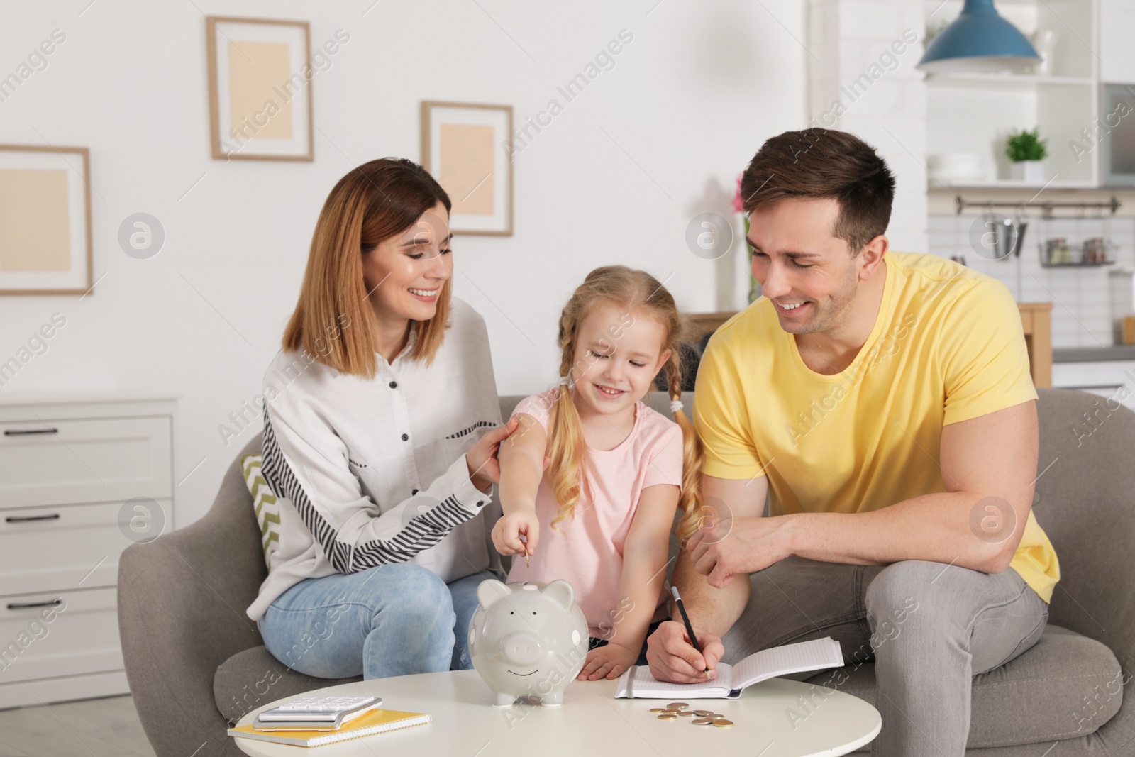 Photo of Happy family putting coin into piggy bank at table indoors. Saving money