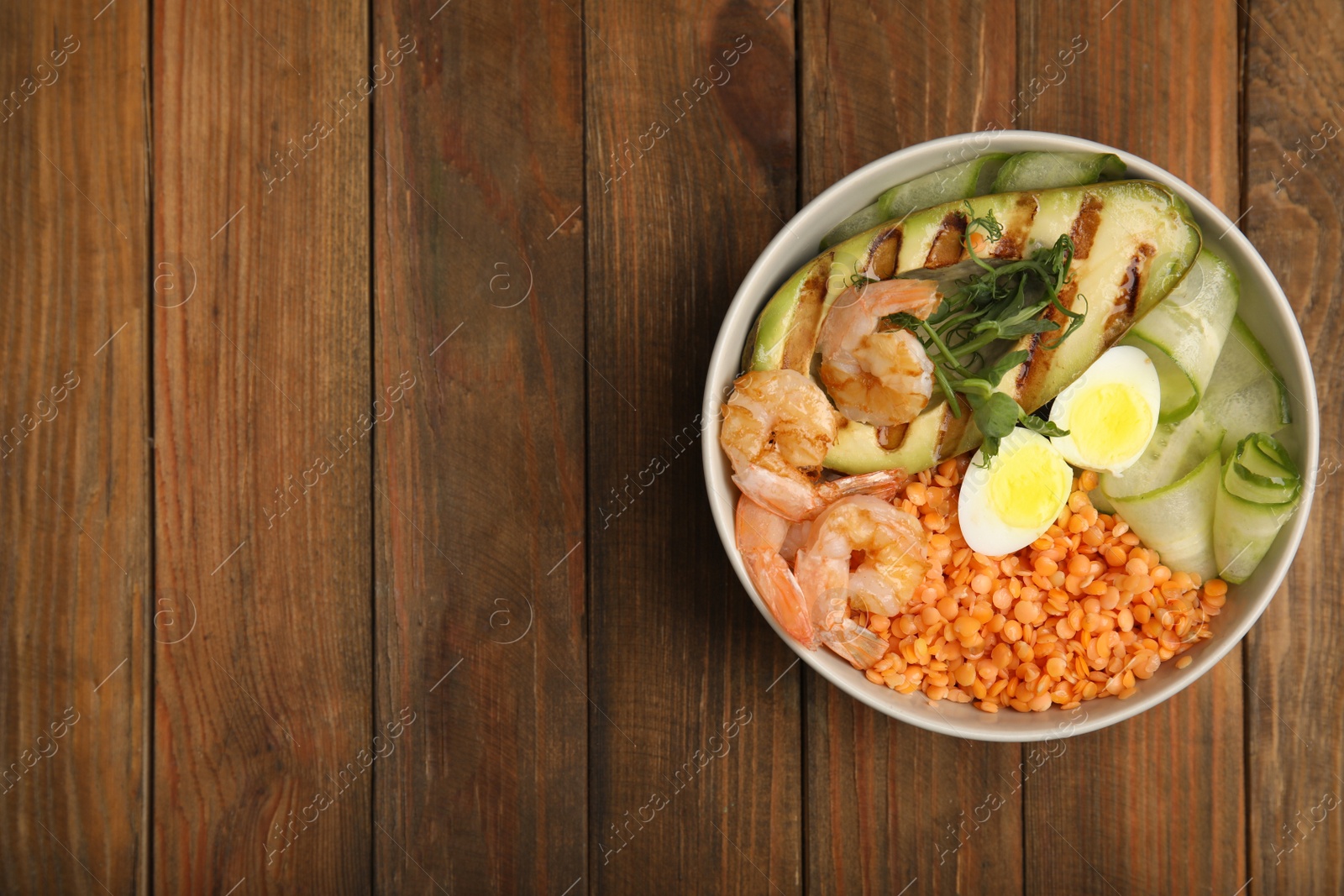 Photo of Delicious lentil bowl with avocado, shrimps, egg and cucumber on wooden table, top view. Space for text