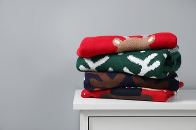 Different folded Christmas sweaters on chest of drawers against grey background. Space for text