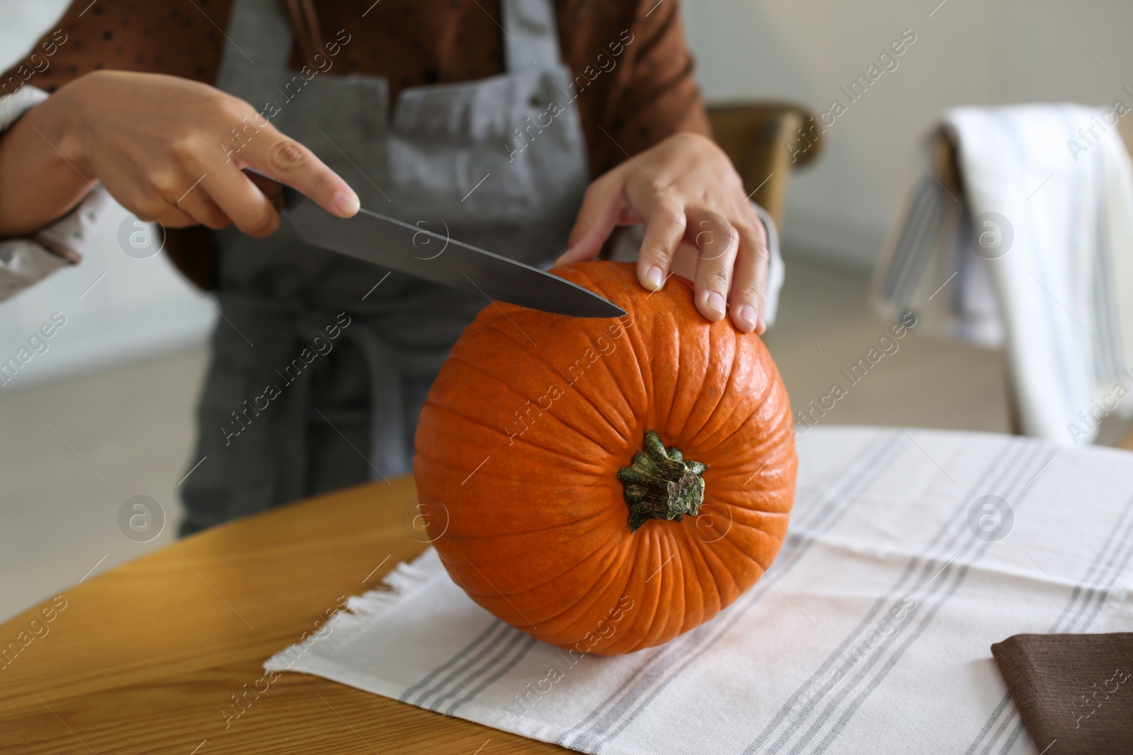 Photo of Woman carving pumpkin at table in kitchen. Halloween celebration